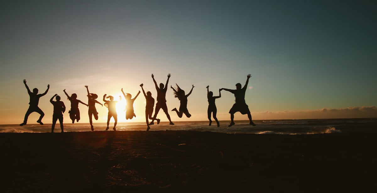 Friends jump in the air as they celebrate being at the beach.